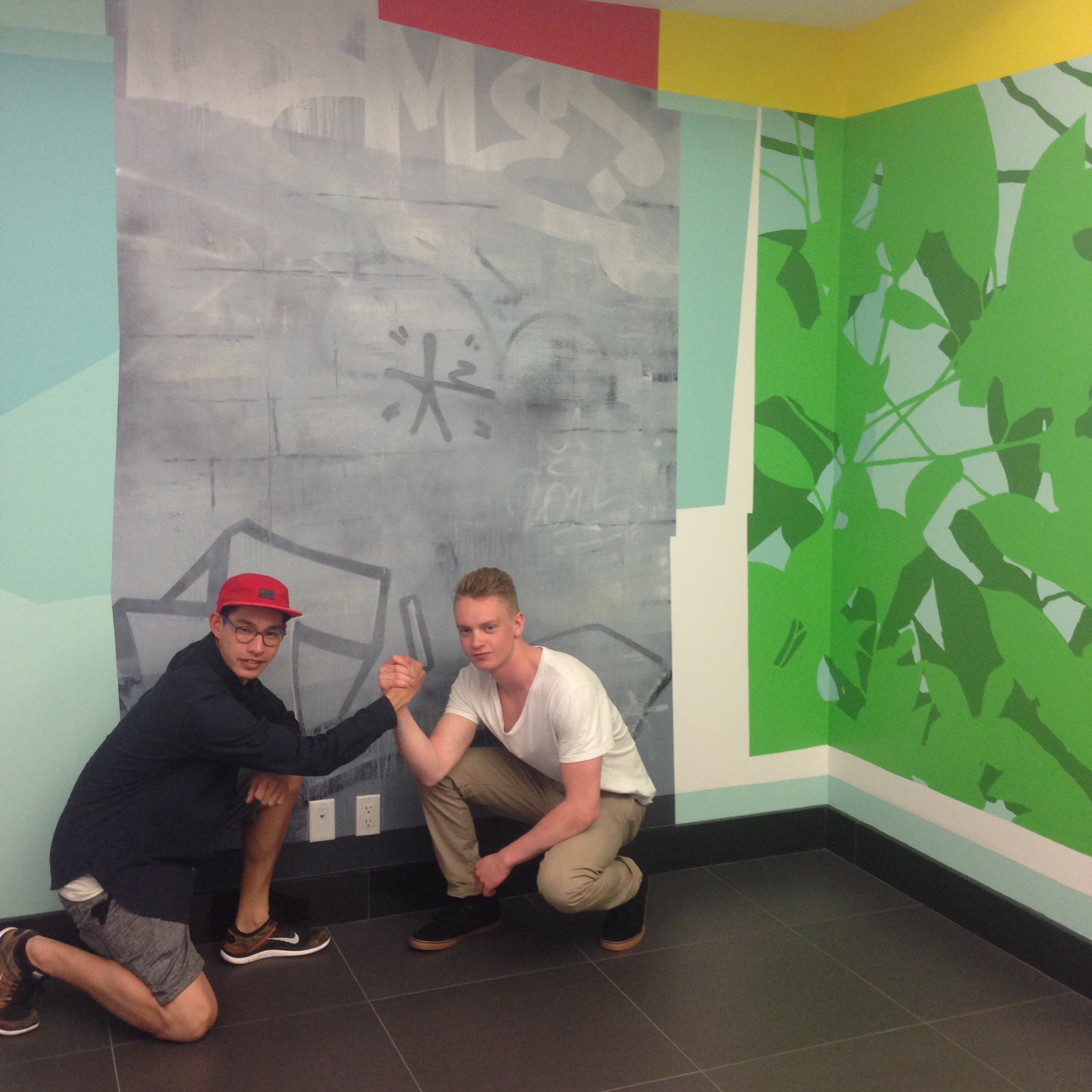 A picture of Michael Rozen and Scott Sueme 2015 artists in residence in front of their mural in the Vancouver office.