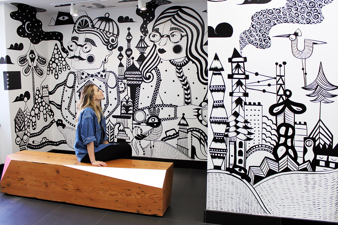 Ola Volo sitting on a bench looking at her finished mural in the hcma Vancouver office lobby.
