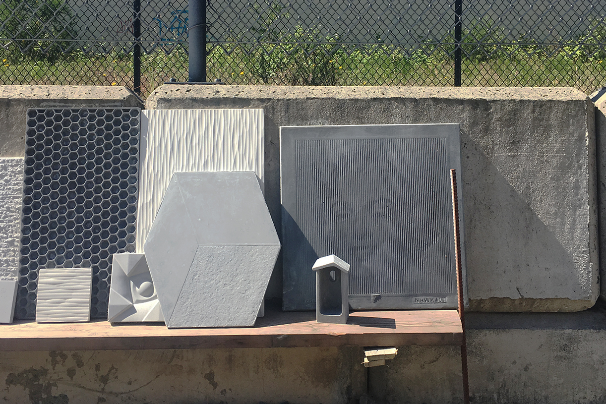 Various sized marble and rock tiles and a small bird house leaning against a fence.