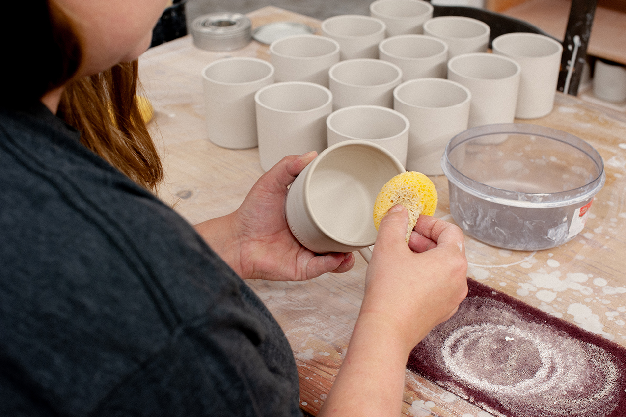 Mindy Doke smoothing moulded ceramic mugs with a sponge and water.