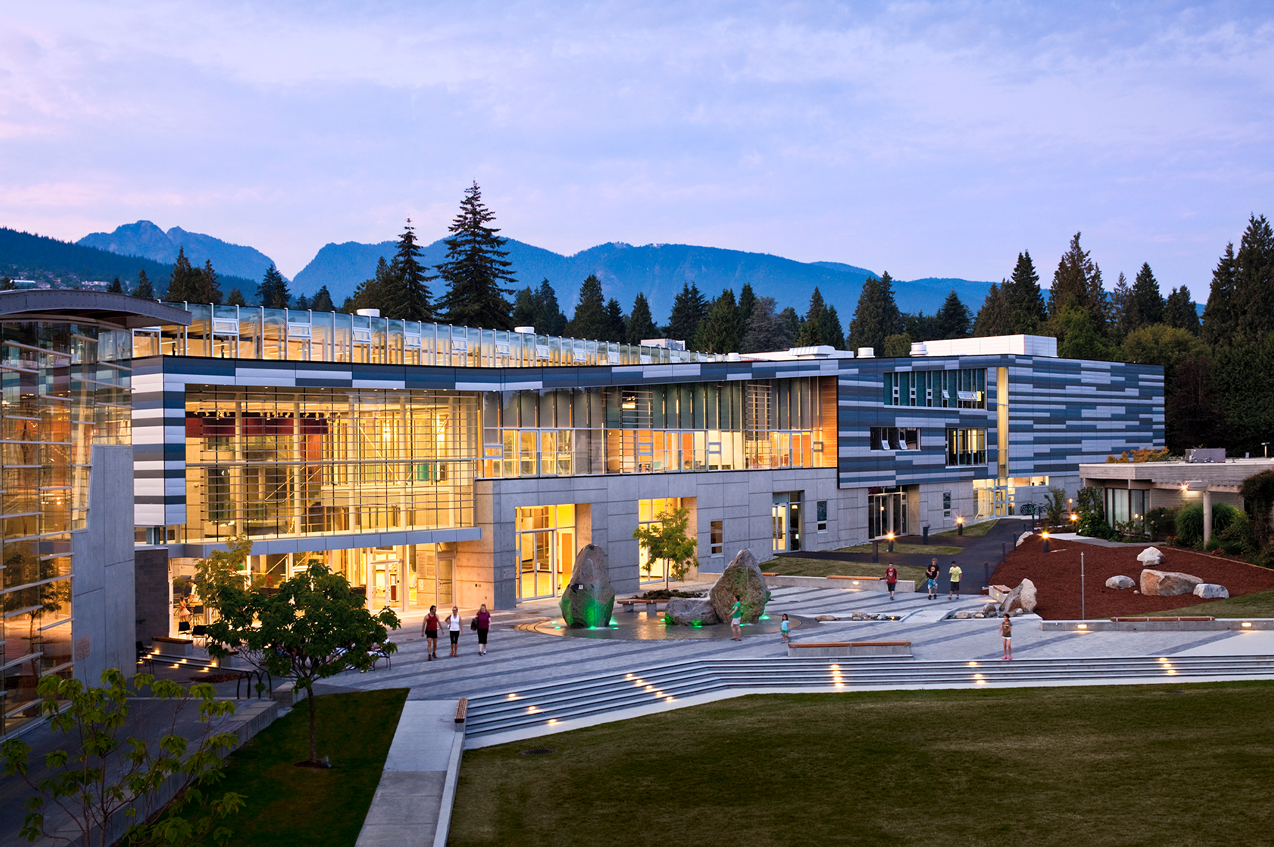 Evening scene of the West Vancouver Community Centre–a large building with a lot of windows and two big rock sculpture at the entrance.