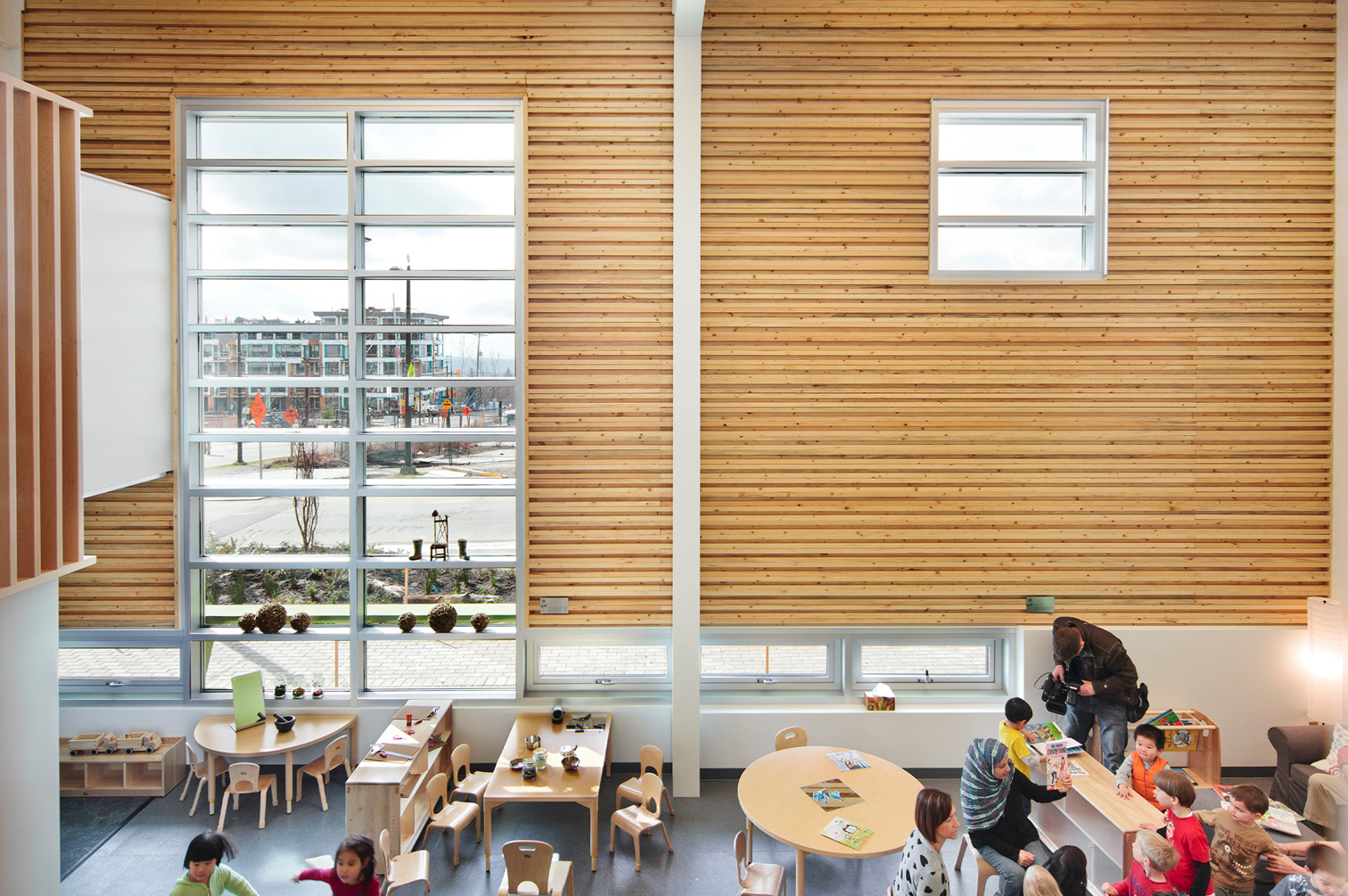 Children in their classroom with high ceilings, a large window and wooden walls.