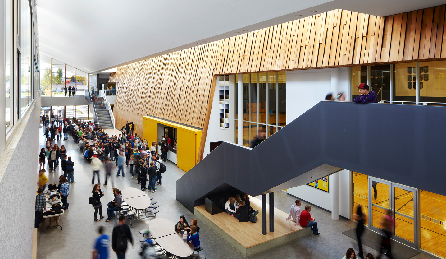 School main hallway with students and geometric staircase and wooden walls.