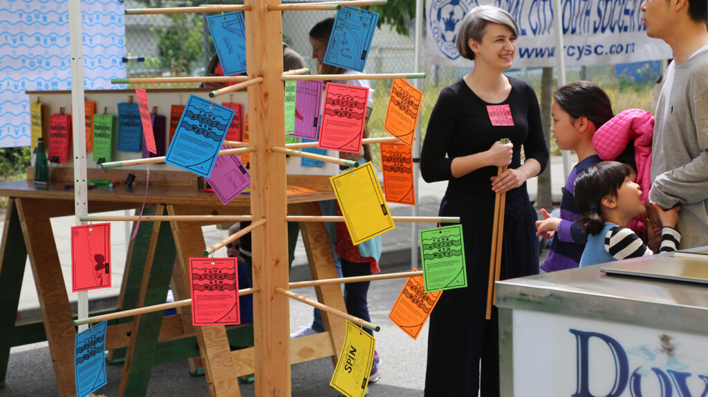 Colourfully designed cards hanging on a rack, while a worker talks to a family.
