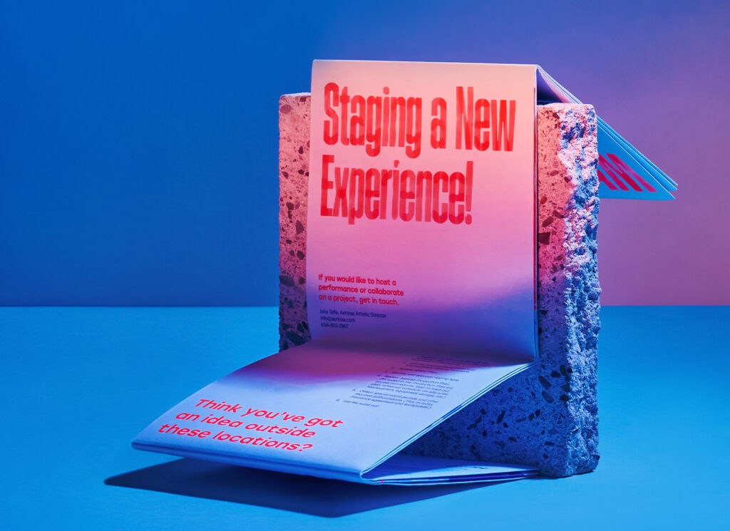 Pamphlet that states "Staging a New Experience!" presented on a concrete block.