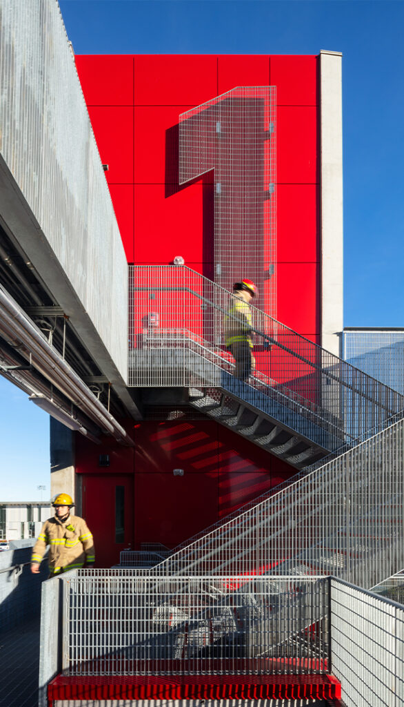 Large red wall with large number one accompanied by firefighters walking down metal staircase