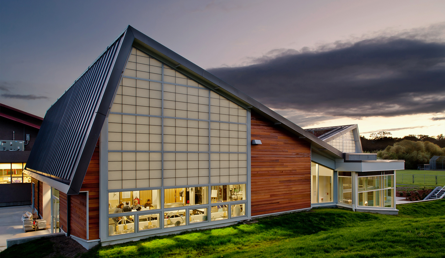 An evening exterior view of Arts Centre at Cedar Hill, a one-storey building with wood panels and angular shapes.