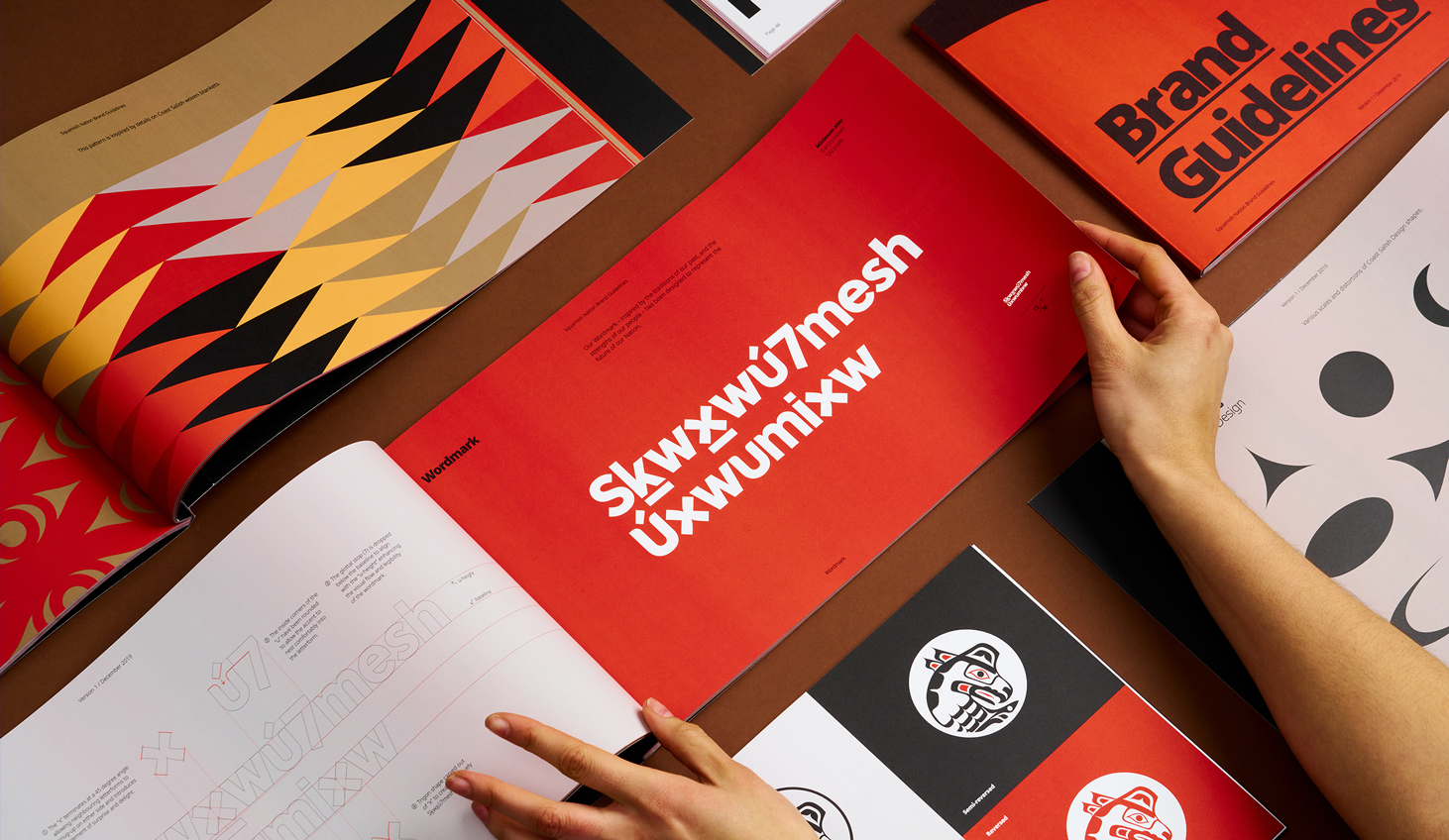 Someone flipping through the Squamish Nation Brand guidelines. It sows the white word mark that says "Skwxwú7mesh Úxwumixw" (Squamish Nation) and a red background.