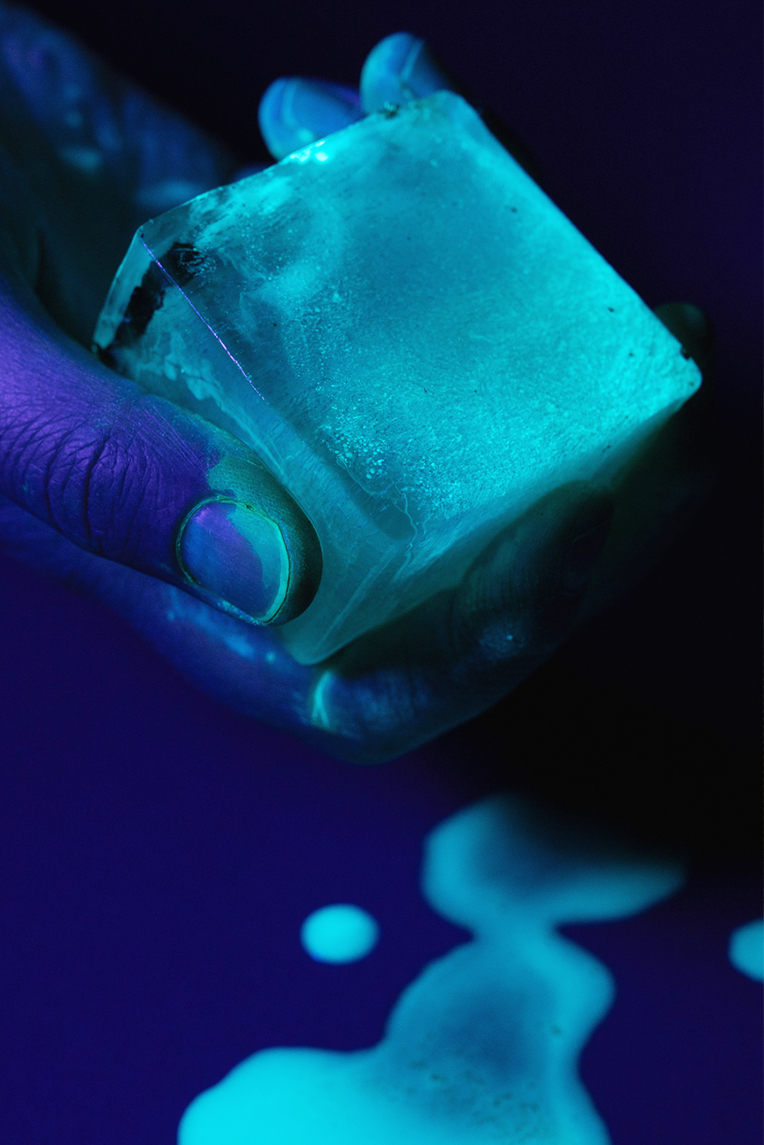 A hand holding a glow-in-the-dark ice cube under UV light.