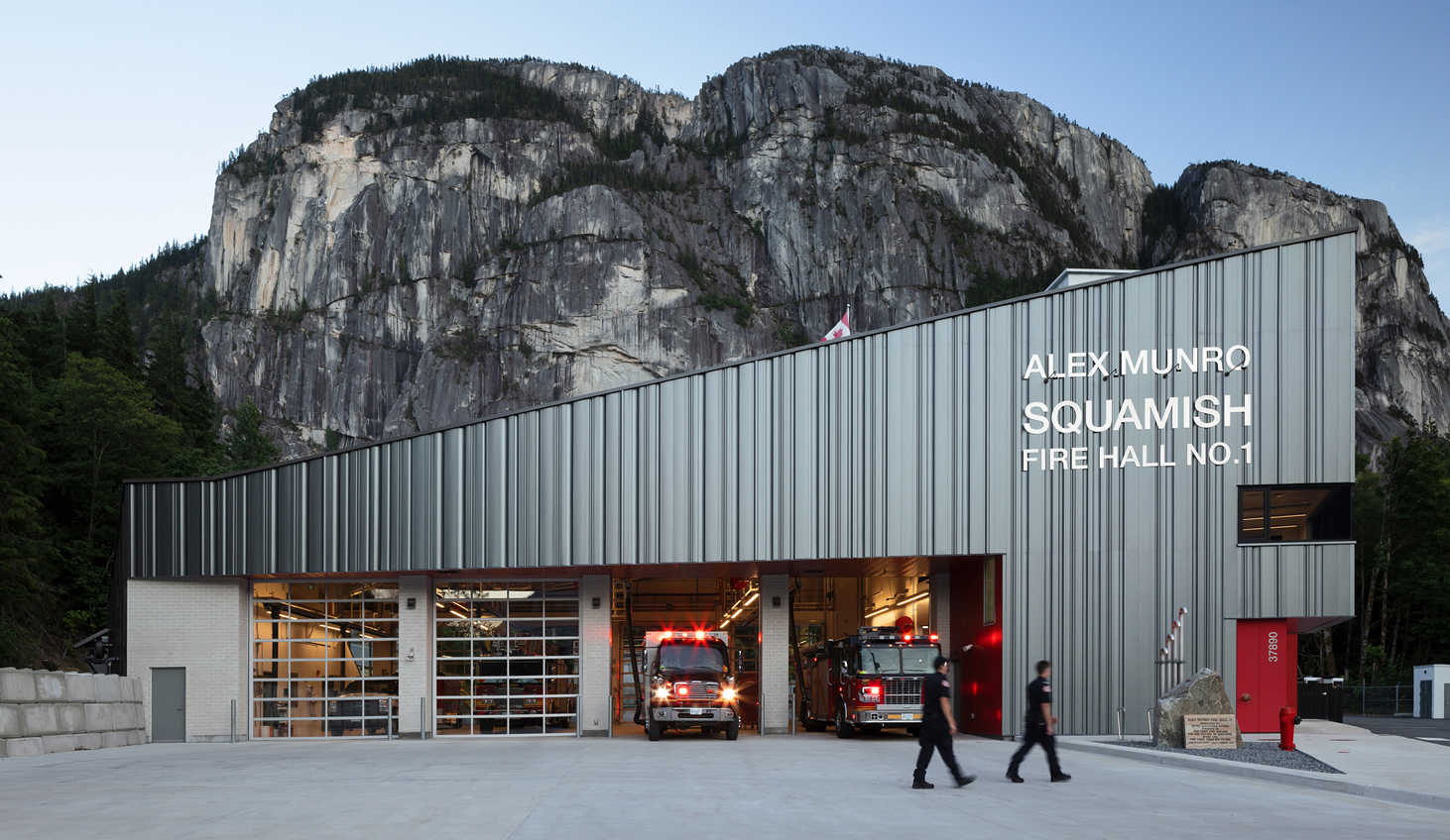 Exterior front view of Squamish Fire Hall No. 1 at dusk. The metal cladded building is framed the Stawamus Chief behind it.