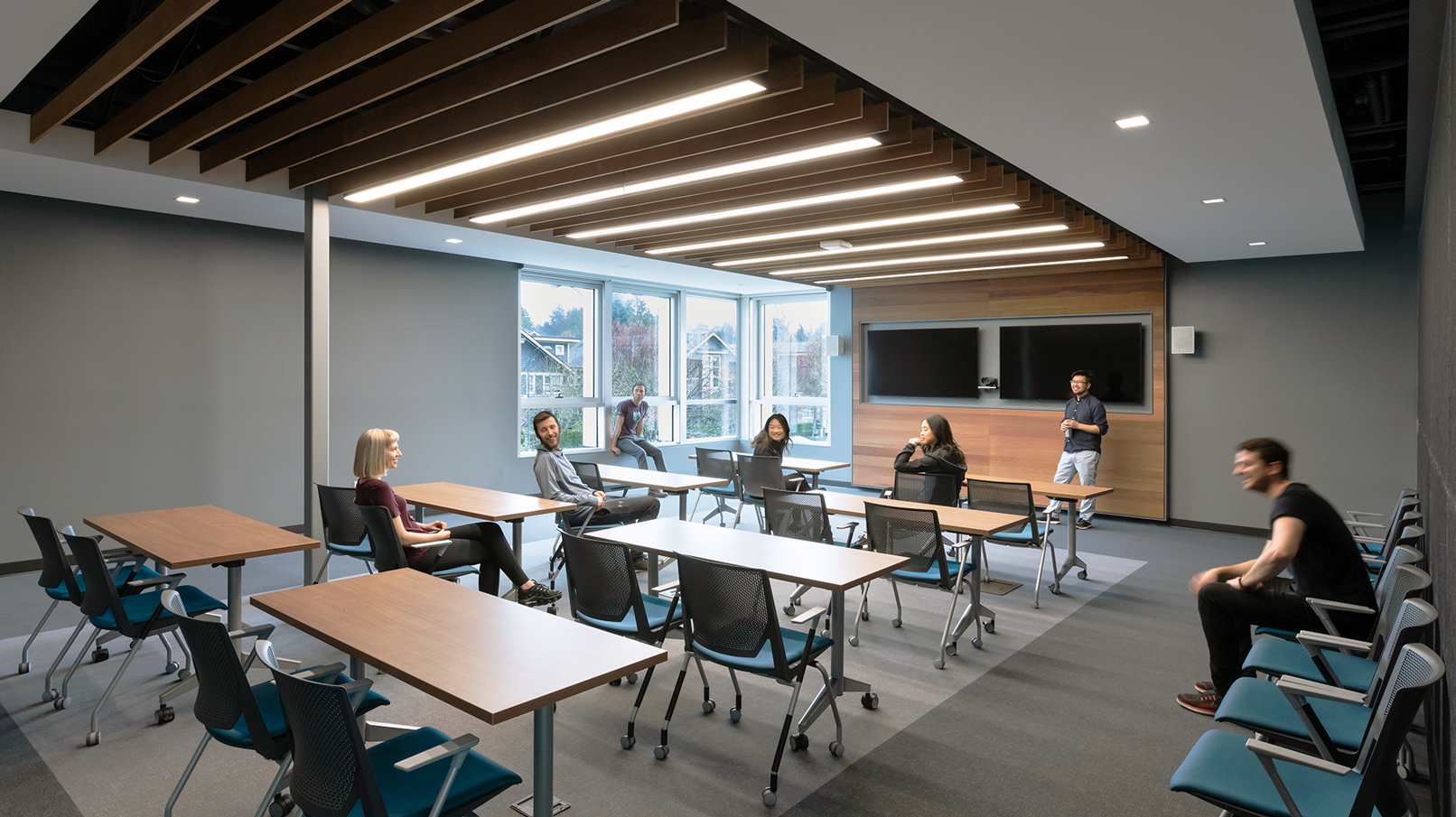 Students sit within a classroom in the pavilion. The desks and chairs all have wheels for flexibility, and there is a wood-slat feature ceiling.