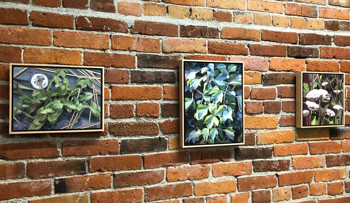 Three framed, oil paintings on panels of yellow weed and small green oak leaves, and green and blue ivy leaves on a brick wall.