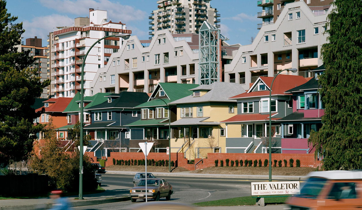 A view of a row of colourful heritage homes with a the building behind them, creating more housing.