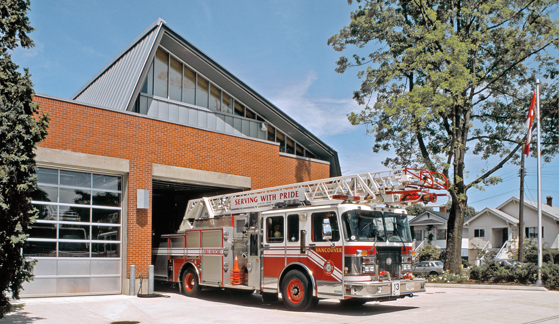 An image of a brick fire hall that has an angular roof and a firetruck parked outside of it.