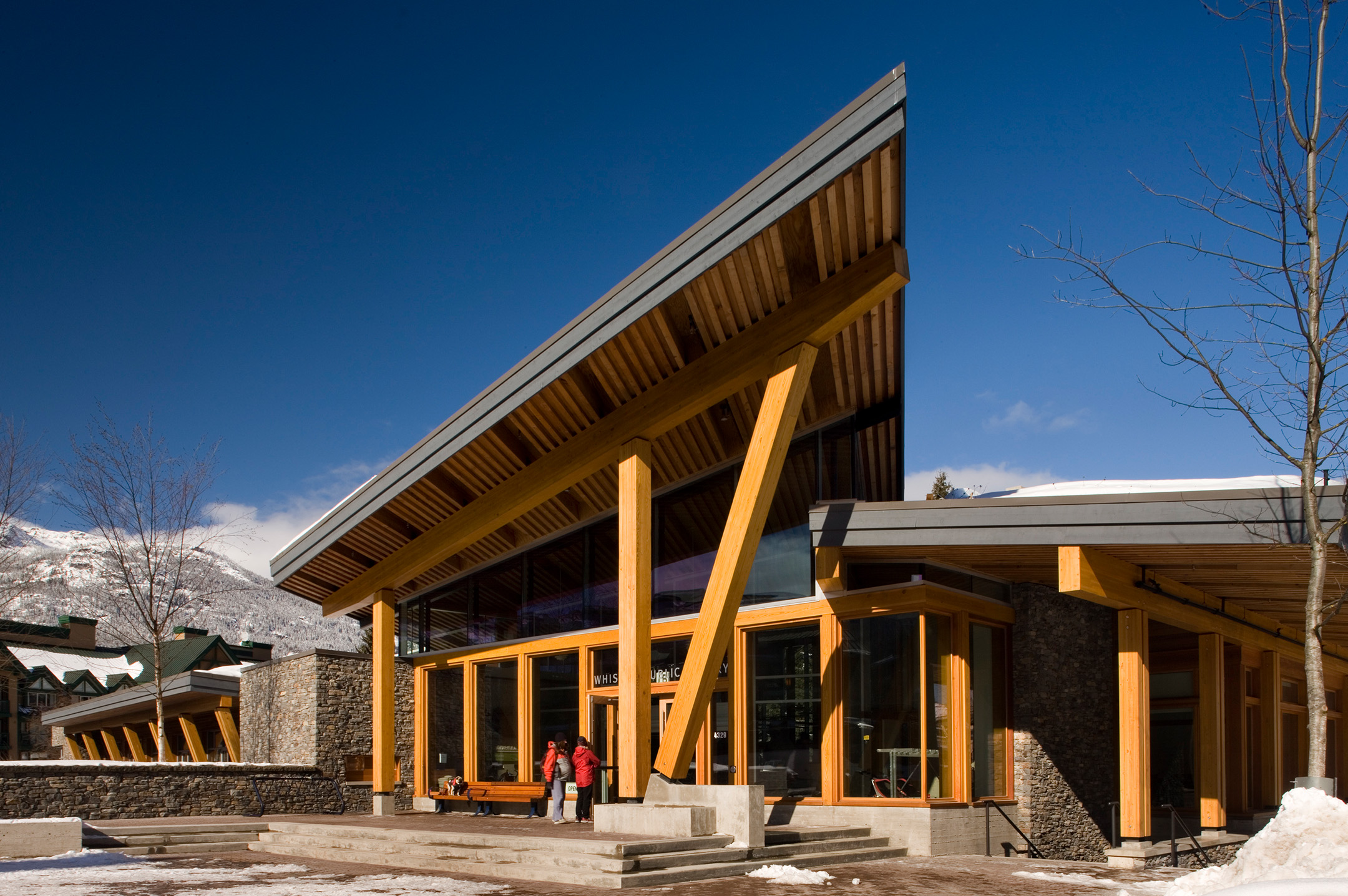 Exterior of the Whistler Public Library, highlighting the mono-pitched roof and wood structure among a mountainous backdrop.