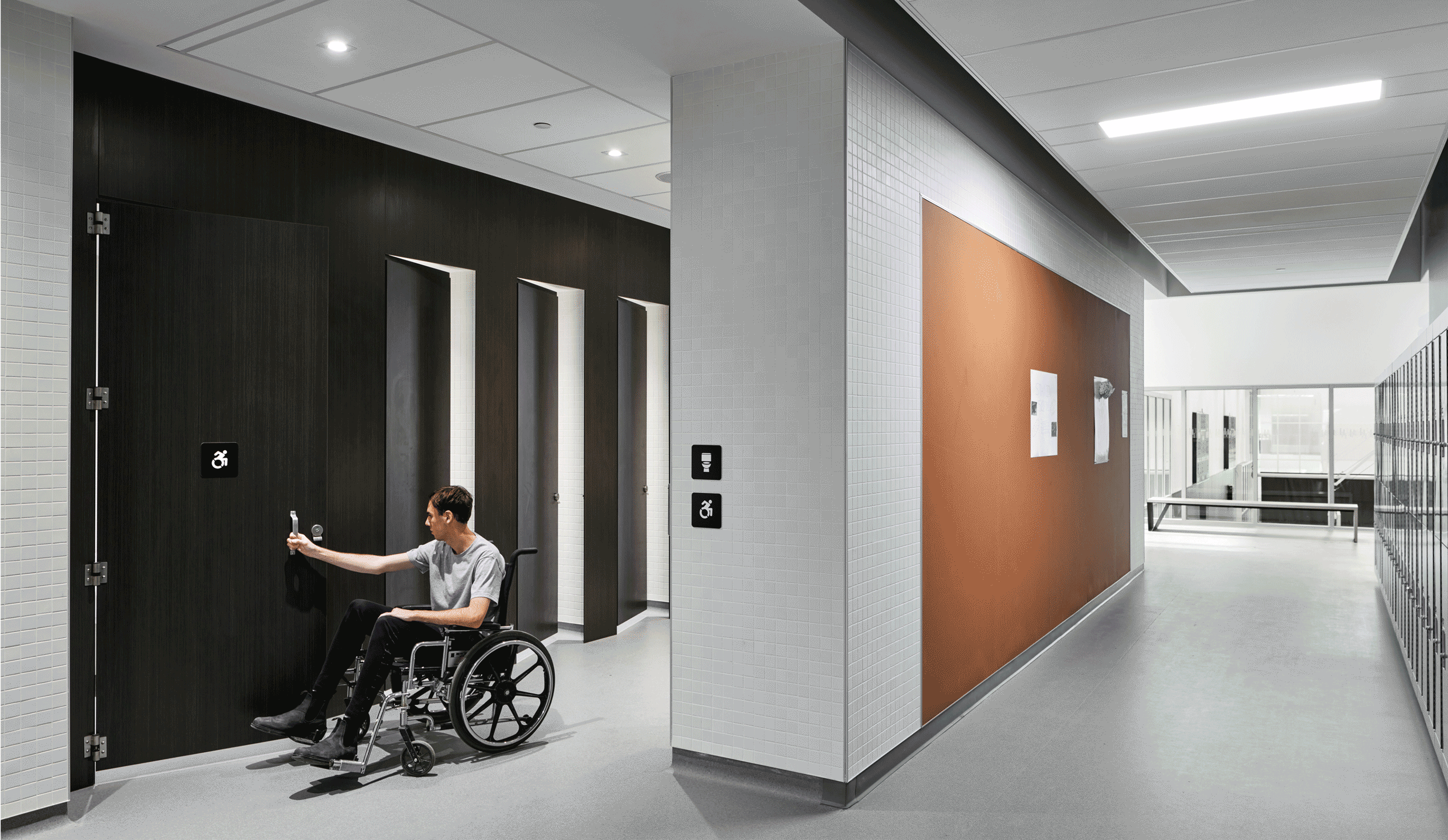 A man using a wheelchair opening the door of an accessible single occupancy stall in an all gender washroom.