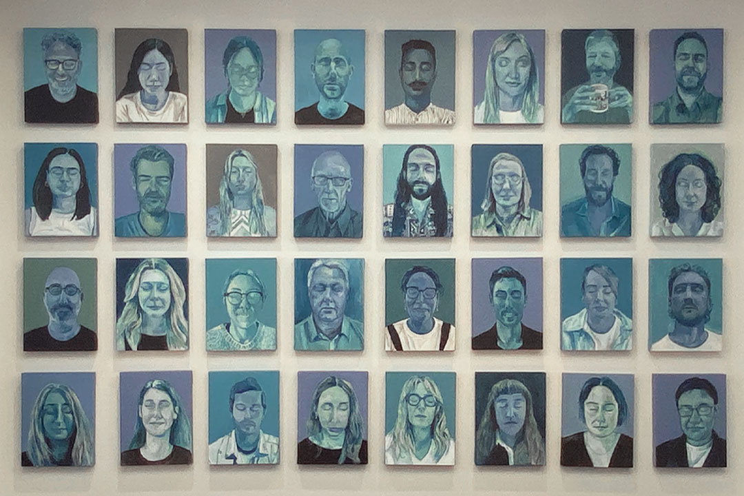 A center close-up of the wall, displaying a section of the 51 blue portraits of people with their eyes closed.