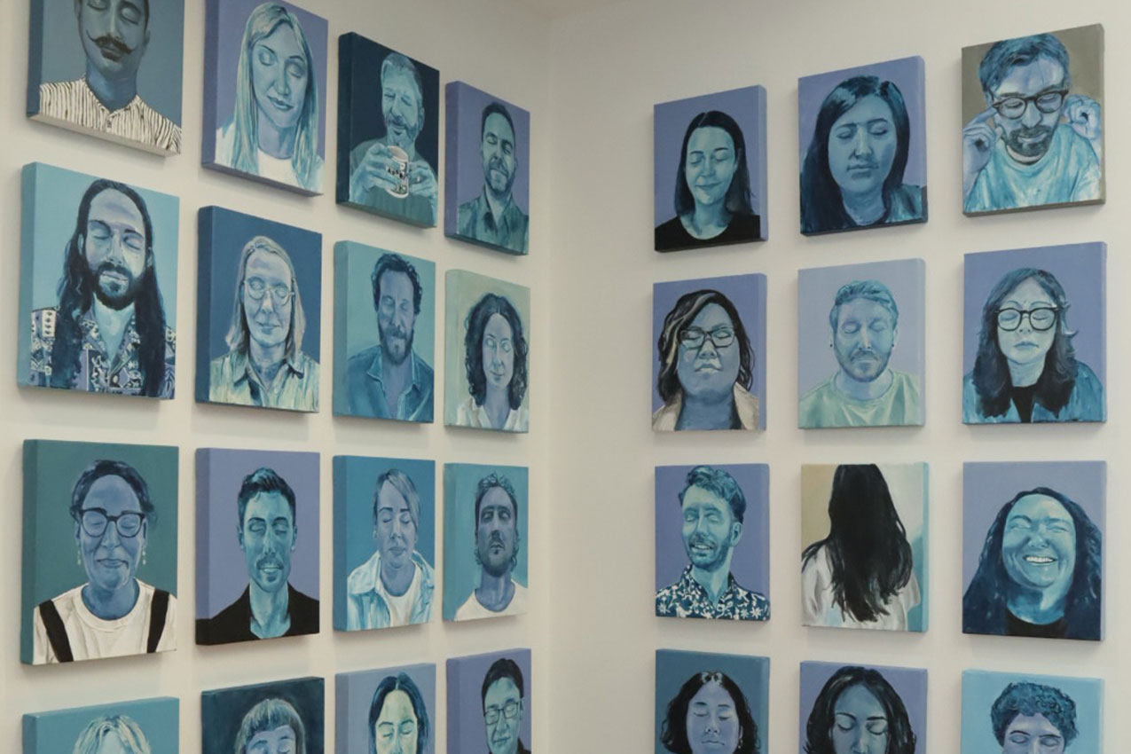 A close-up of the wall, displaying a section of the 51 blue portraits of people with their eyes closed.