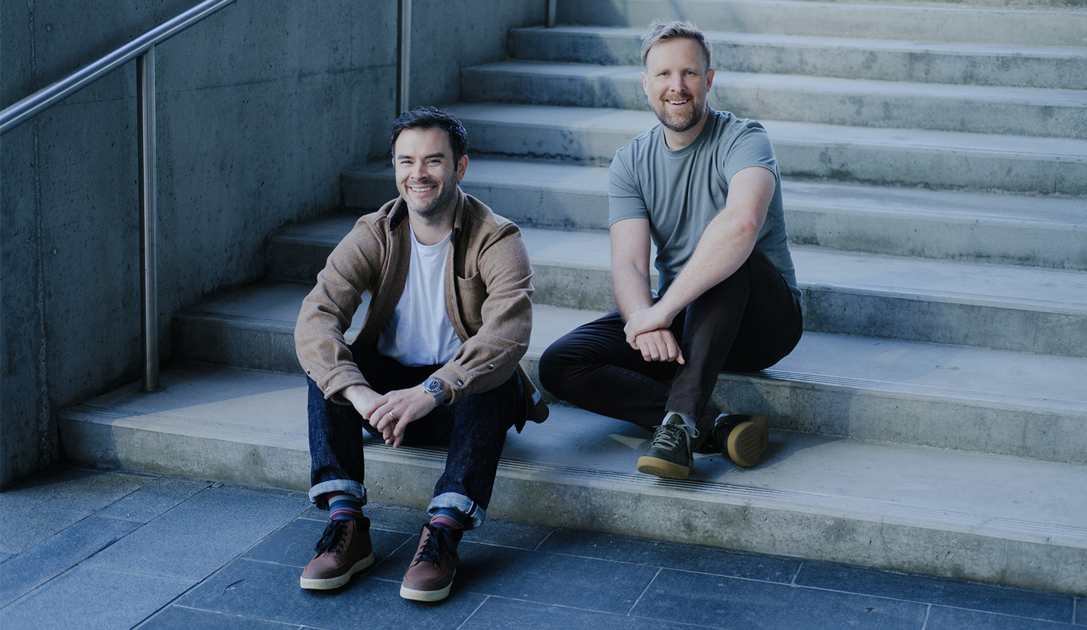 Corey and Rob sit casually together on concrete steps.