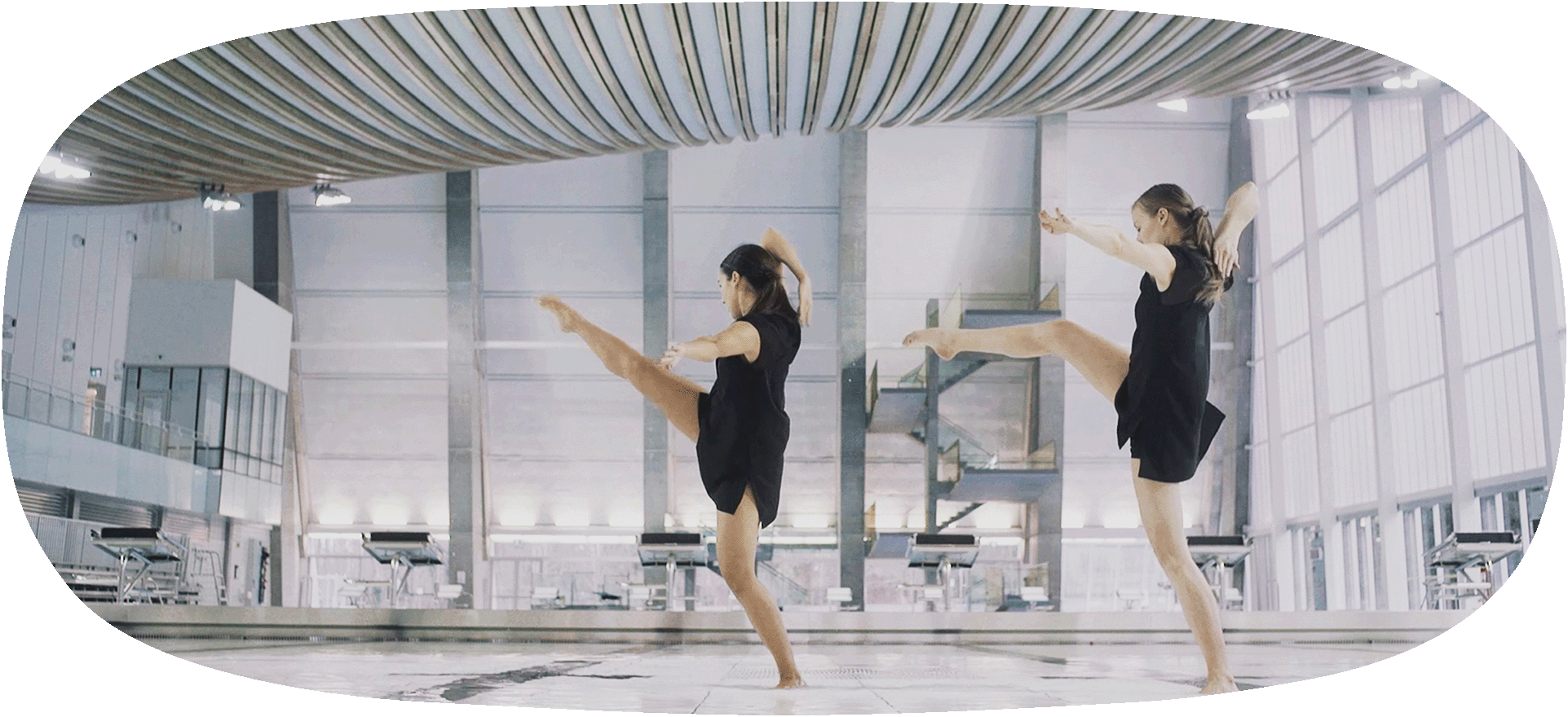 A still frame from the Solid Liquid Ether film, a choreographed dance shot in hcma's project, Grandview Heights Aquatic Centre. The dancers stand with their feet in the water with their legs and arms in action, under Grandview's striking timber catenary roof.