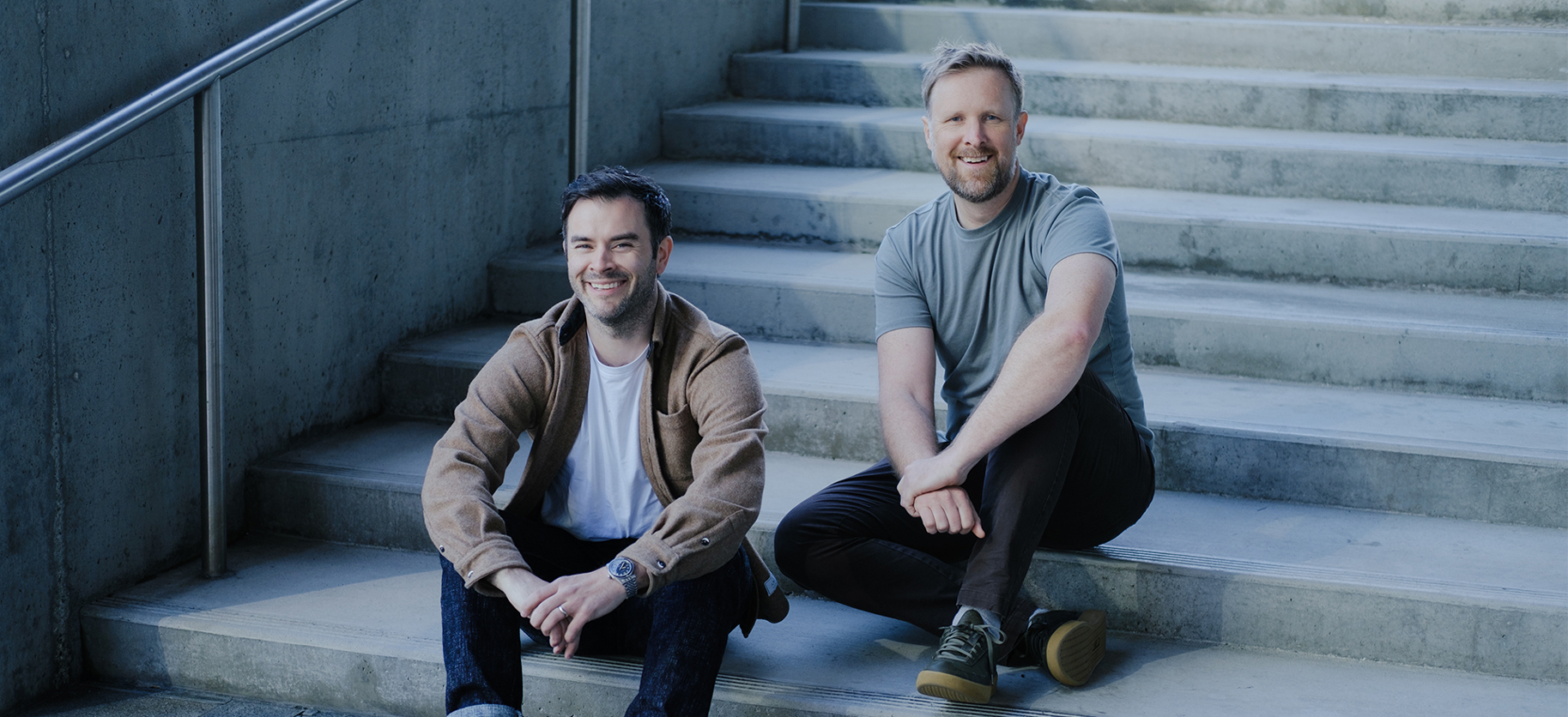Rob and Corey sit casually together on concrete steps.