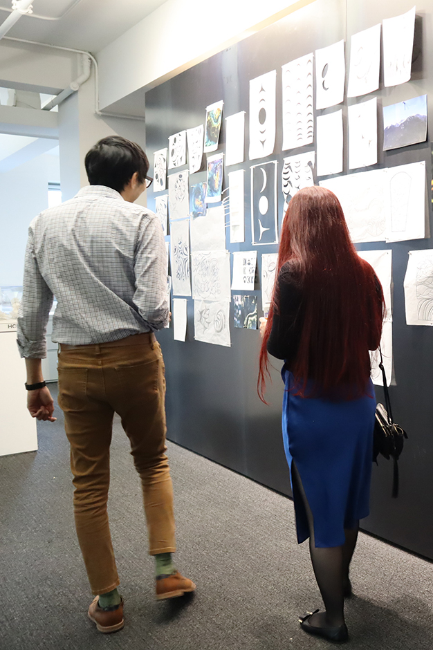 Two people walk side by side, looking at materials from James Harry's residency, pinned up on the magnetic wall of our Vancouver office.