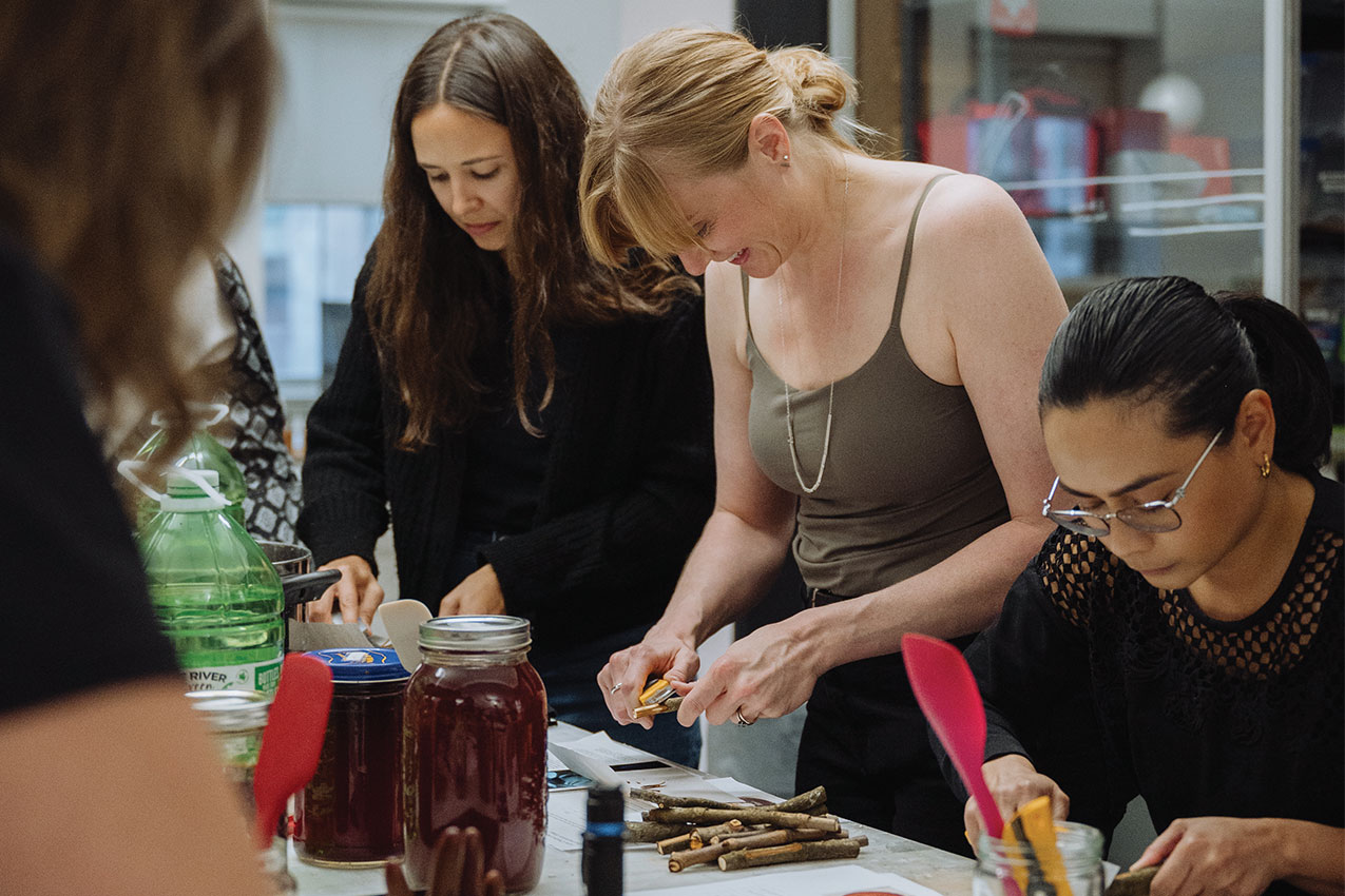 People stand around a table shaving wood off of a twig from a horse chestnust tree, as part of one of Marni Bowman's residency workshops.