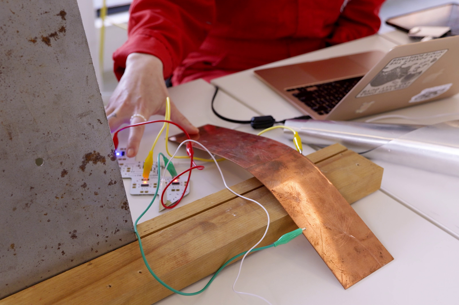 Close crop of Edie interacting with their equipment. Their hand is touching a circuit board with green, yellow, red, and white wires strewn about.