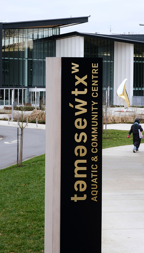 Exterior signage with the facility in the background. A person is walking along a sidewalk to the right.