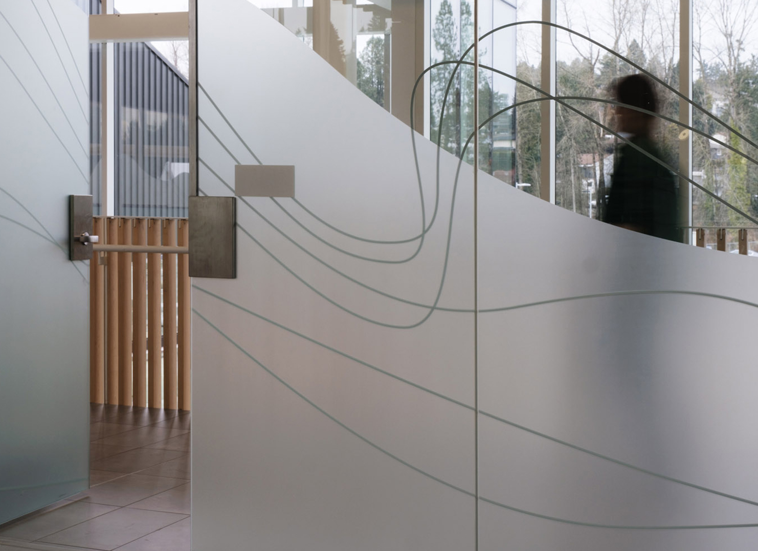 Wavy visibility graphics on a glass wall, with a blurred figure passing down the hallway behind them.